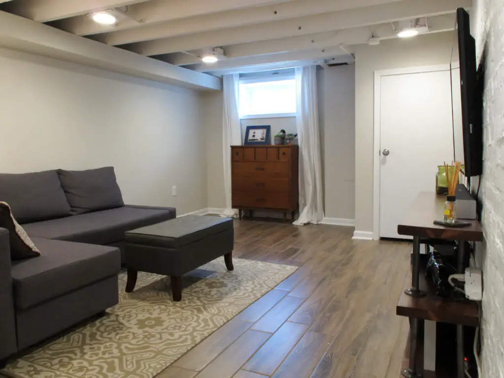 Simple basement remodel with exposed joists and faux wood tile flooring.