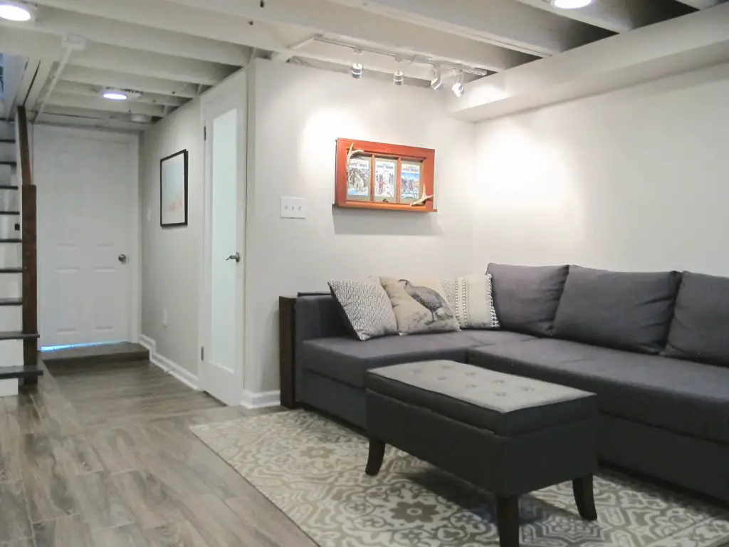 Bright and beautiful basement remodel. Exposed floor joists painted white, faux wood tile floors, privacy glass bathroom door, and painted stairs. | EffieRow.com