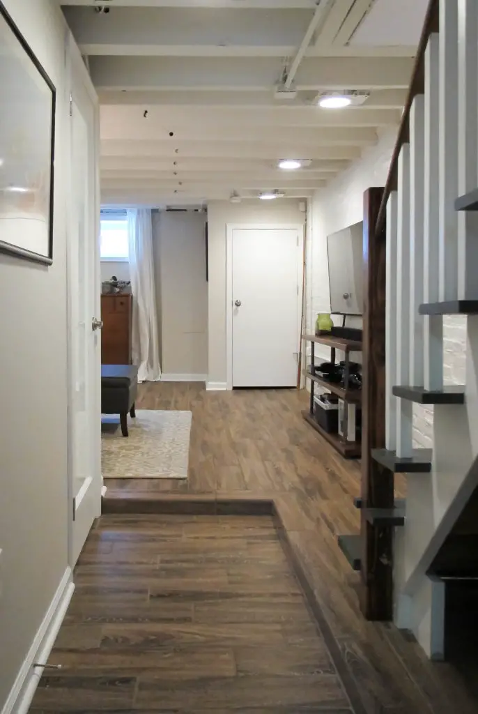 Cozy and chic basement renovation with exposed floor joists and faux wood tils.